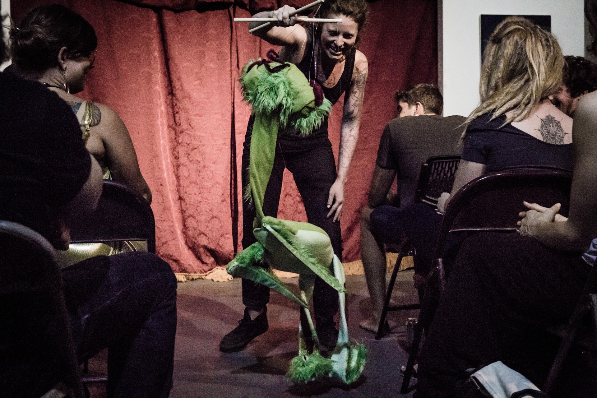 Person leads a large puppet through an indoor audience of adults.